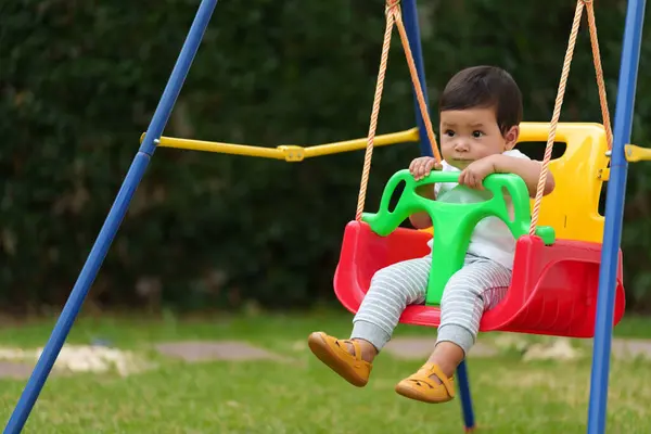 infant baby is playing in a swing in the garden