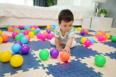 Bebek bebek, yatak odasındaki yapboz minderinde renkli plastik toplar oynuyor.