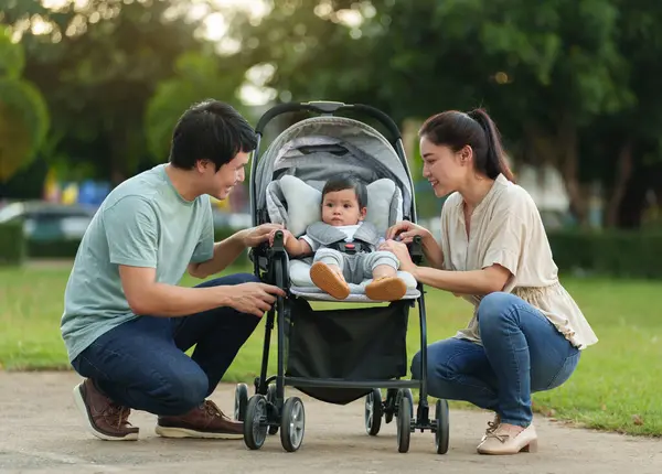 happy parent (father and mother) talking and playing with infant baby in the stroller while resting in park