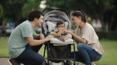 Mutlu ebeveyn (anne ve baba) parkta dinlenirken bebek arabasında bebek bebekle konuşuyor ve onunla oynuyor.