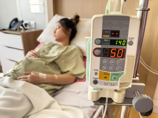 automatic infusion IV drip saline pump machine with pregnant woman resting on a bed in hospital
