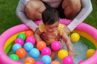 Mutlu baba ve bebek bebek havuzda renkli plastik toplarla su sıçratmaca oynuyorlar.