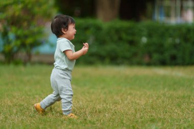 Ağlayan bebek parkta yeşil çimlerin üzerinde yürümeyi öğreniyor.