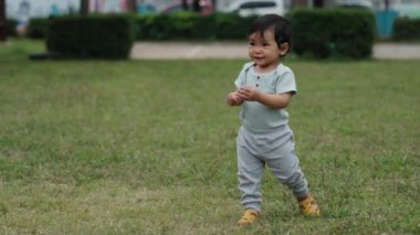 Mutlu bebek parkta yeşil çimlerin üzerinde ilk adım atmayı öğreniyor.