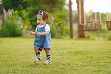 Bebek parkta yeşil çimlerin üzerinde ilk adım atmayı öğreniyor.