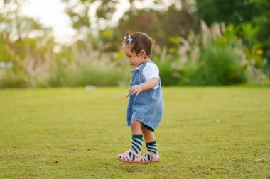 Bebek parkta yeşil çimlerin üzerinde ilk adım atmayı öğreniyor.