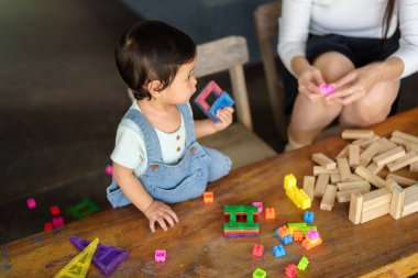 Yürüyen kız, annesiyle masada oyuncak oynuyor.