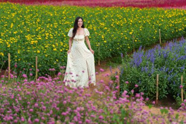 Elbise giymiş güzel bir kadın Bahçedeki çiçek tarlasının tadını çıkarıyor
