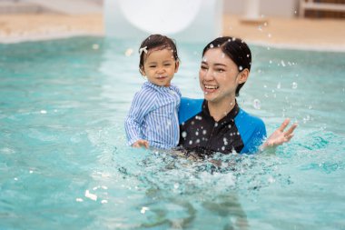 Mutlu anne, yüzme havuzunda su sıçratma oyunu oynarken bebeği kollarında tutuyor.