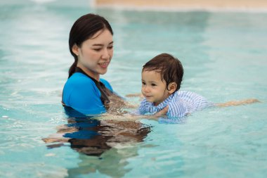 Mutlu anne kızına havuzda yüzmeyi öğretiyor.