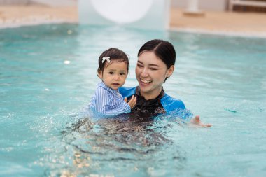 Mutlu anne yüzme havuzunda oynarken bebeği kollarında tutuyor.