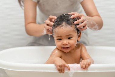 Anne banyo yapıyor ve bebek saçlarını şampuanla yıkıyor. 
