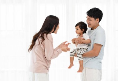 Neşeli anne ve baba, beyaz pencere arkasında bebekle sarılıp oynuyorlar. Mutlu aile kavramı