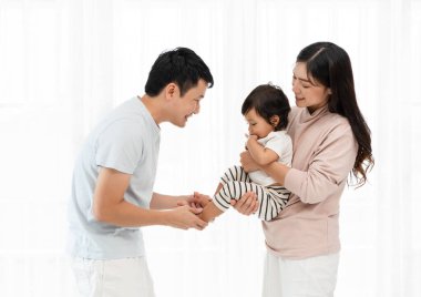 Neşeli anne ve baba, beyaz pencere arkasında bebekle sarılıp oynuyorlar. Mutlu aile kavramı