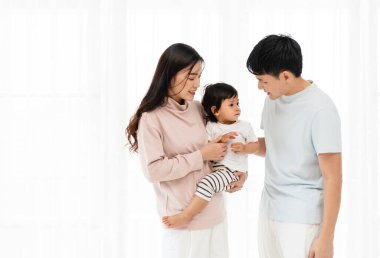 Neşeli bir anne ve baba, beyaz bir pencerede bebekle sarılıp sohbet ediyorlar. Mutlu aile kavramı