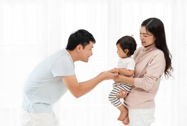 Neşeli anne ve baba, beyaz pencere arkasında bebekle sarılıp oynuyorlar. Mutlu aile kavramı