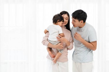 Neşeli bir anne ve baba, beyaz bir pencerede bebekle sarılıp sohbet ediyorlar. Mutlu aile kavramı