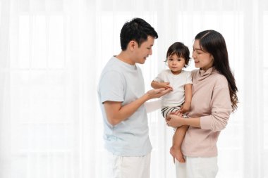 Neşeli bir anne ve baba, beyaz bir pencerede bebekle sarılıp sohbet ediyorlar. Mutlu aile kavramı