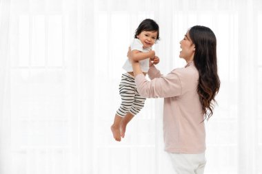 Mutlu anne kucağında ve küçük bebeğiyle beyaz pencere arkasında kaldırırken