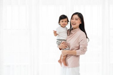 Mutlu anne kucağında bebekle beyaz pencerenin arkasında