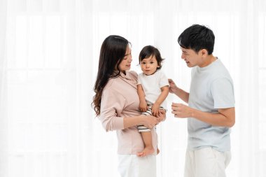 Neşeli bir anne ve baba, beyaz bir pencerede bebekle sarılıp sohbet ediyorlar. Mutlu aile kavramı