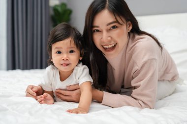 Mutlu anne yalan söylüyor ve bebeğiyle yatakta oynuyor.