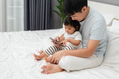 Babasıyla yeni yürümeye başlayan bebek yatakta akıllı telefon kullanıyor.