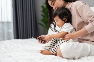 Bebekle anne yatakta akıllı telefon kullanıyor.