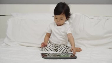 Bebek yatakta dijital tablet kullanıyor ve izliyor.