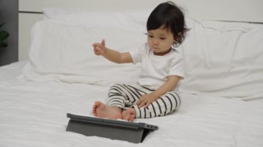 Bebek yatakta dijital tablet kullanıyor ve izliyor.