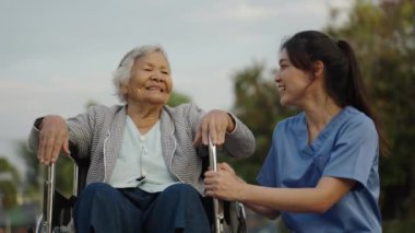 Mutlu hemşire, parkta tekerlekli sandalyedeki yaşlı kadın hastayla ilgileniyor ve onunla konuşuyor.