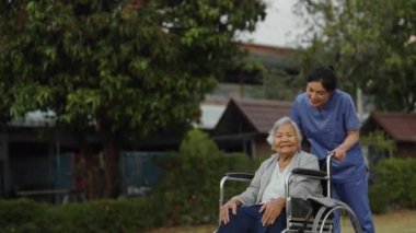 Hemşire, parkta tekerlekli sandalyedeki yaşlı bayanla ilgileniyor ve onunla ilgileniyor.