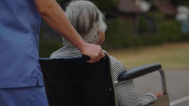 Hemşire, parkta tekerlekli sandalyedeki yaşlı bayanla ilgileniyor ve onunla ilgileniyor.