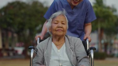 Hemşire, parkta tekerlekli sandalyedeki yaşlı bayanla ilgileniyor ve onunla ilgileniyor.
