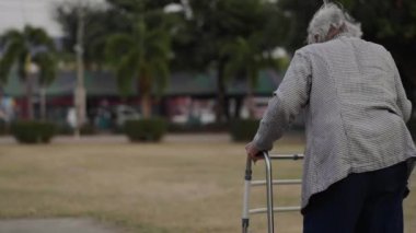 Yaşlı kadın parkta Walker 'la yürüyor.