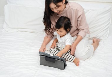 Bebekle anne yatakta dijital tablet bilgisayar kullanıyor.