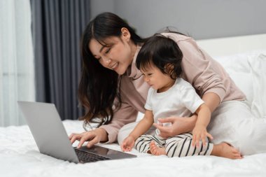 Bebekle anne yatakta dizüstü bilgisayar kullanıyor.