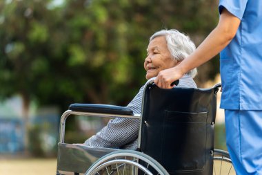 Hemşire, parkta tekerlekli sandalyedeki mutlu yaşlı kadına göz kulak ol.
