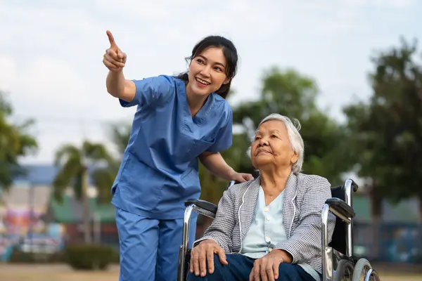 happy caregiver nurse take care and talking with senior woman in using walker at the park