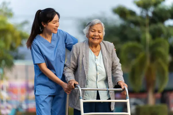 caregiver nurse support senior woman walking with walker in the park