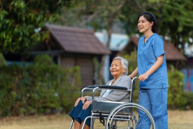Mutlu hemşire, parkta tekerlekli sandalyedeki yaşlı bayanla ilgileniyor ve onu itiyor.
