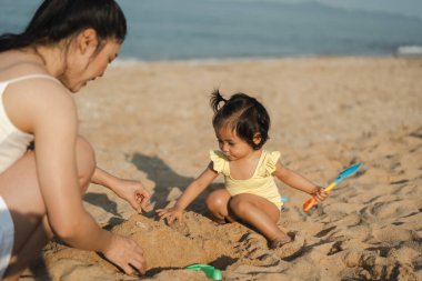 Mutlu küçük kız annesiyle kumsalda kum oyuncağı oynuyor.
