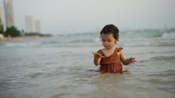 幸せなトッドラーの赤ん坊の女の子は海岸で砂と水を遊んで ストック動画