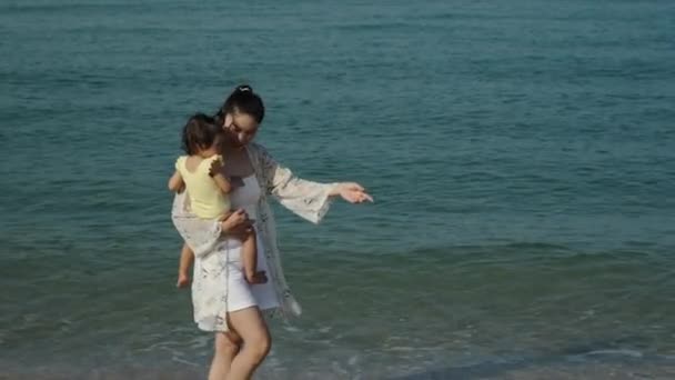 在海滩上 妈妈慢慢地抱着她那蹒跚学步的女婴 和她一起散步 免版税图库视频