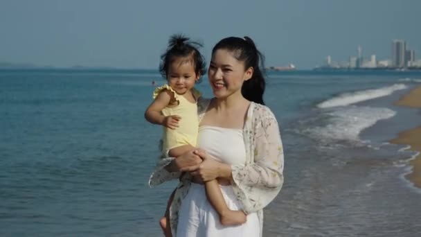 快乐的妈妈慢吞吞地抱着她那蹒跚学步的女婴在海滩上奔跑 免版税图库视频片段