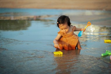 Mutlu bebek kız deniz sahilinde oyuncak ve su oynuyor.