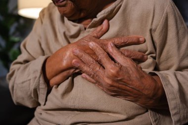 close up senior woman suffering from bad pain in her chest heart while sitting on a sofa in the living room at night clipart