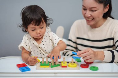 Anne küçük kızına masada ahşap eğitim geometrisi oynamayı öğretiyor.