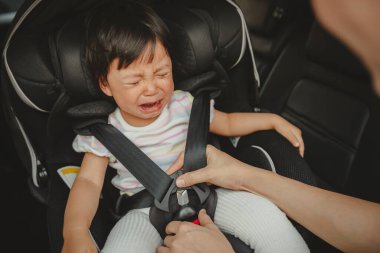 Baba emniyet kemerini bebek koltuğunda ağlayan bebeğe bağlıyor.