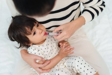 Anne, bebeğe şırıngayla sıvı ilaç veriyor. Hasta çocuk.